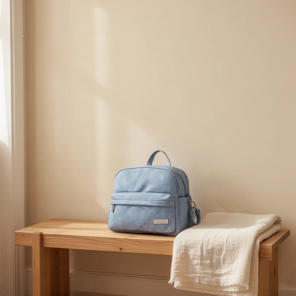 Sac à dos à langer compact effet cuir posé sur un banc dans une entrée