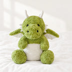 Dragon moelleux en peluche 30 cm posé sur un lit blanc, en pleine lumière