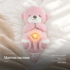 Peluche loutre qui respire rose sur fond crème, en studio. Marron ou rose : veilleuse au ventre, 3 piles AAA, sans câble