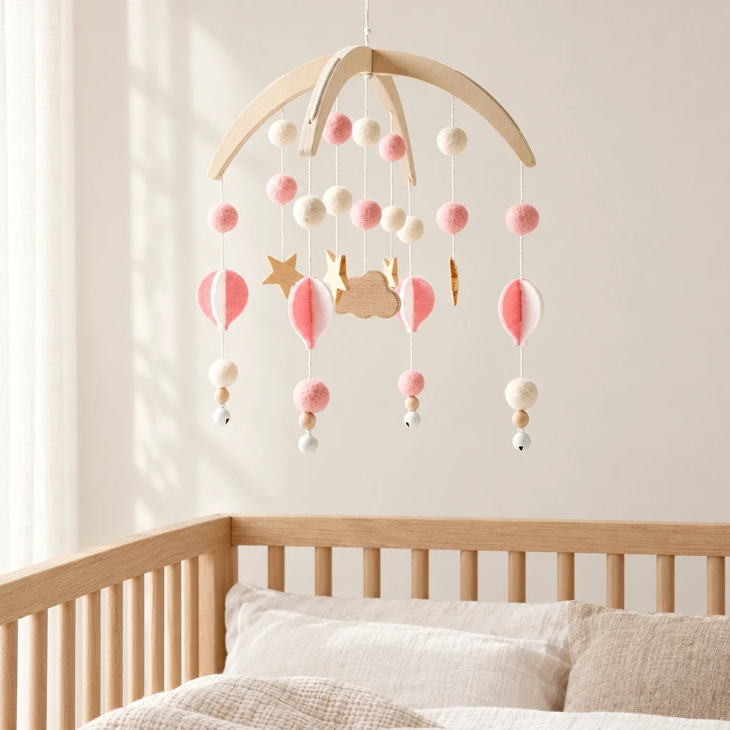 Mobile Bébé Bohème Rose en bois suspendu au-dessus d’un lit bébé en bois clair, dans une chambre douce