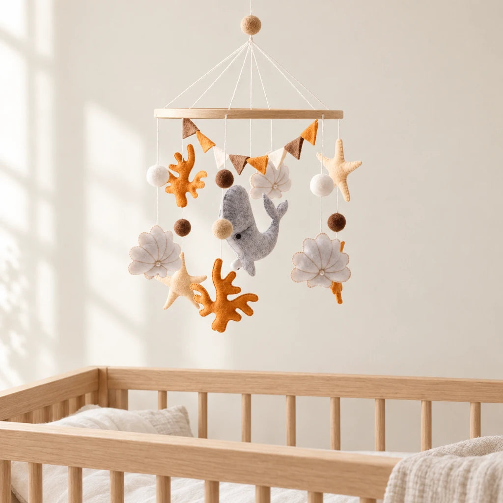 Mobile Bébé Corail en bois suspendu au-dessus d’un lit bébé en bois clair, dans une chambre douce