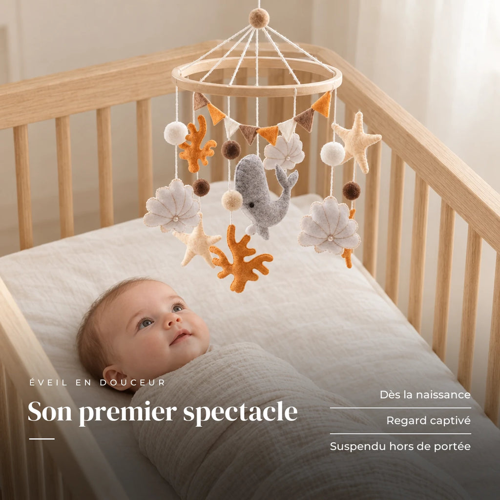 Bébé allongé dans son lit qui regarde le mobile bébé Corail en bois au-dessus de lui. Son premier spectacle : dès la naissance, regard captivé, suspendu hors de portée