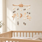 Mobile Bébé Crépuscule en bois suspendu au-dessus d’un lit bébé en bois clair, dans une chambre douce