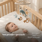 Bébé allongé dans son lit qui regarde le mobile bébé Fonds marins en bois au-dessus de lui. Son premier spectacle : dès la naissance, regard captivé, suspendu hors de portée