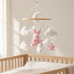 Mobile bébé Lapin rose en bois suspendu au-dessus d’un lit bébé en bois clair, dans une chambre douce