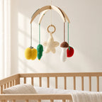 Mobile Bébé Légumes en bois suspendu au-dessus d’un lit bébé en bois clair, dans une chambre douce