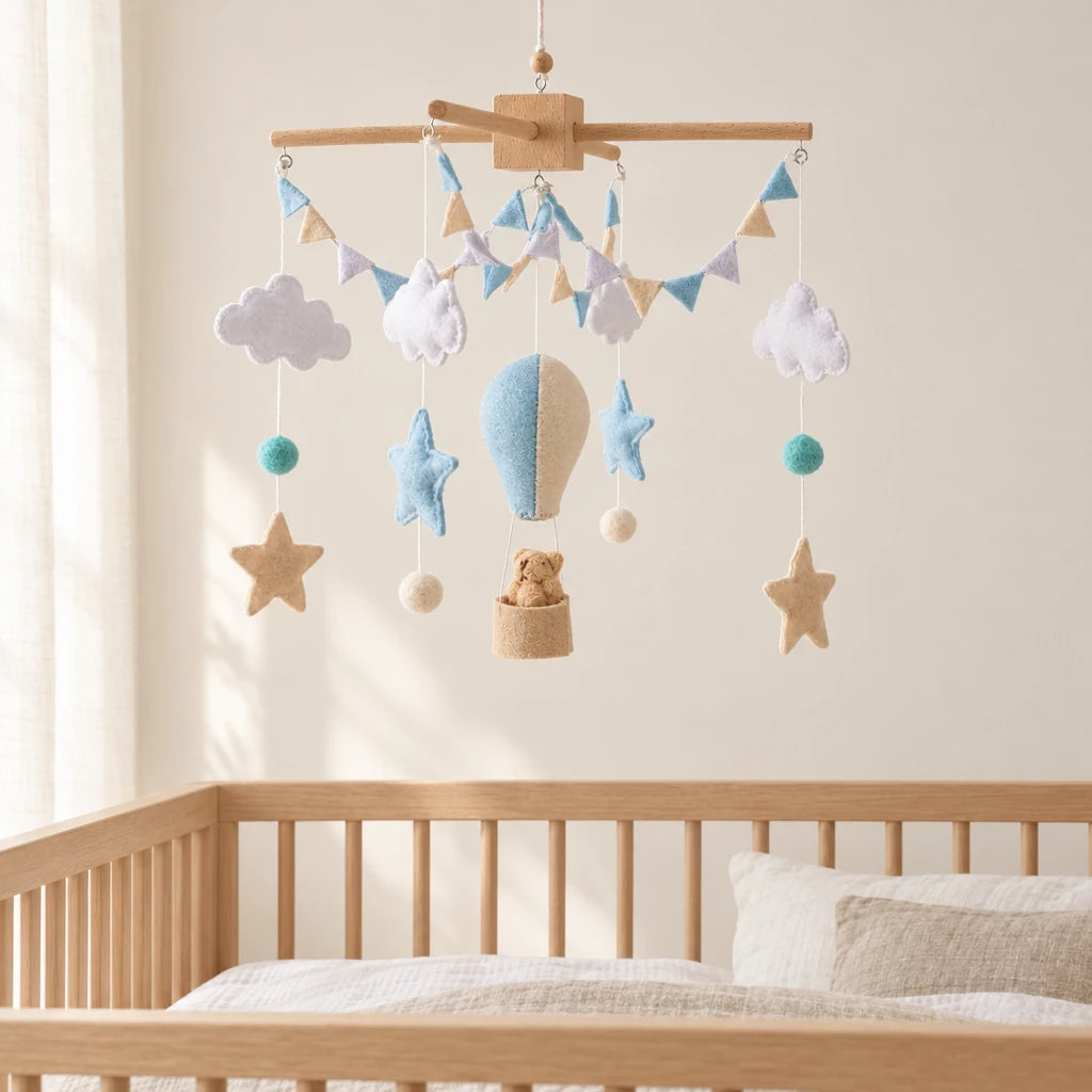 Mobile Bébé Montgolfière bleue en bois suspendu au-dessus d’un lit bébé en bois clair, dans une chambre douce