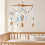 Mobile Bébé Montgolfière bleue en bois suspendu au-dessus d’un lit bébé en bois clair, dans une chambre douce