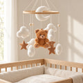 Mobile bébé Nounours en bois suspendu au-dessus d’un lit bébé en bois clair, dans une chambre douce