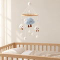 Mobile Bébé Nuage en bois suspendu au-dessus d’un lit bébé en bois clair, dans une chambre douce