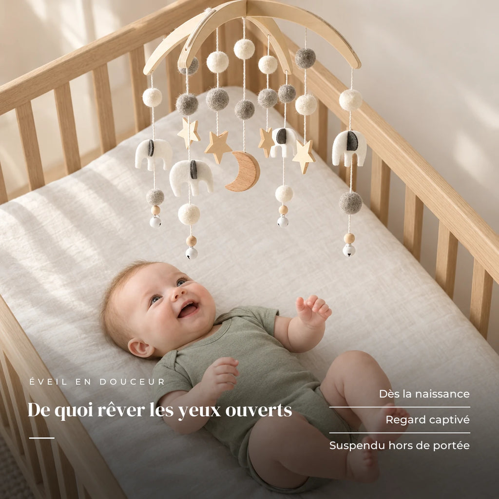 Bébé allongé dans son lit qui regarde le mobile bébé Nuit en bois au-dessus de lui. De quoi rêver les yeux ouverts : dès la naissance, regard captivé, suspendu hors de portée