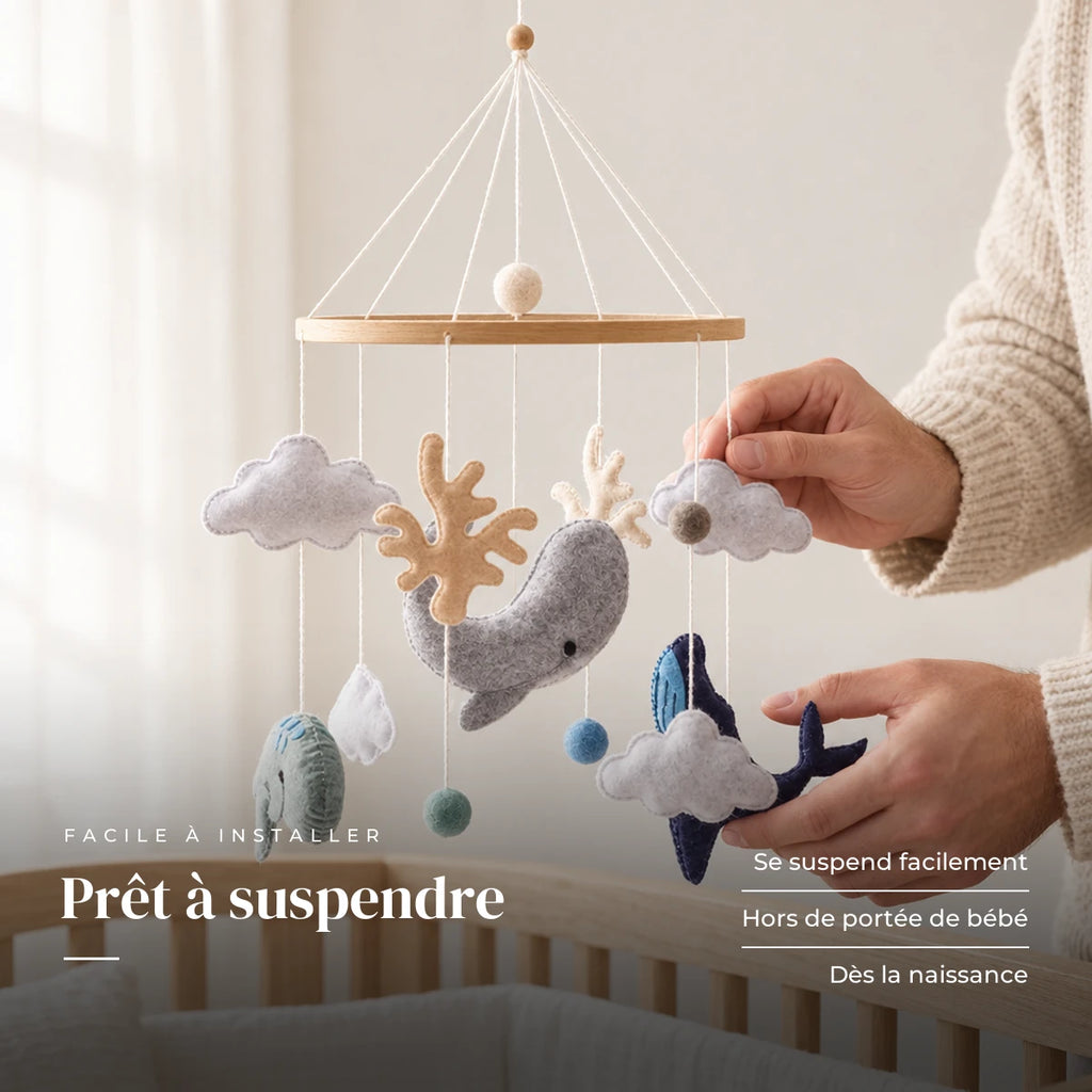 Un parent ajuste une suspension du mobile bébé Océan en bois au-dessus du lit. Prêt à suspendre : se suspend facilement, hors de portée de bébé, dès la naissance