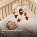 Bébé allongé dans son lit qui regarde le mobile bébé Ourson Lune en bois au-dessus de lui. Son premier spectacle : dès la naissance, regard captivé, suspendu hors de portée