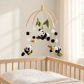 Mobile bébé Panda en bois suspendu au-dessus d’un lit bébé en bois clair, dans une chambre douce