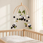 Mobile bébé Panda en bois suspendu au-dessus d’un lit bébé en bois clair, dans une chambre douce
