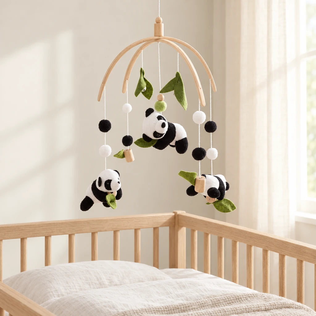 Mobile bébé Panda en bois suspendu au-dessus d’un lit bébé en bois clair, dans une chambre douce