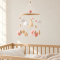 Mobile Bébé Petit Mouton rose en bois suspendu au-dessus d’un lit bébé en bois clair, dans une chambre douce