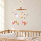 Mobile Bébé Petit Mouton rose en bois suspendu au-dessus d’un lit bébé en bois clair, dans une chambre douce