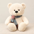 Ours en peluche géant brun avec son écharpe blanc sur fond crème, en studio