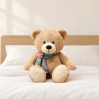 Ours en peluche géant brun avec son écharpe sable posé sur un lit en lin blanc