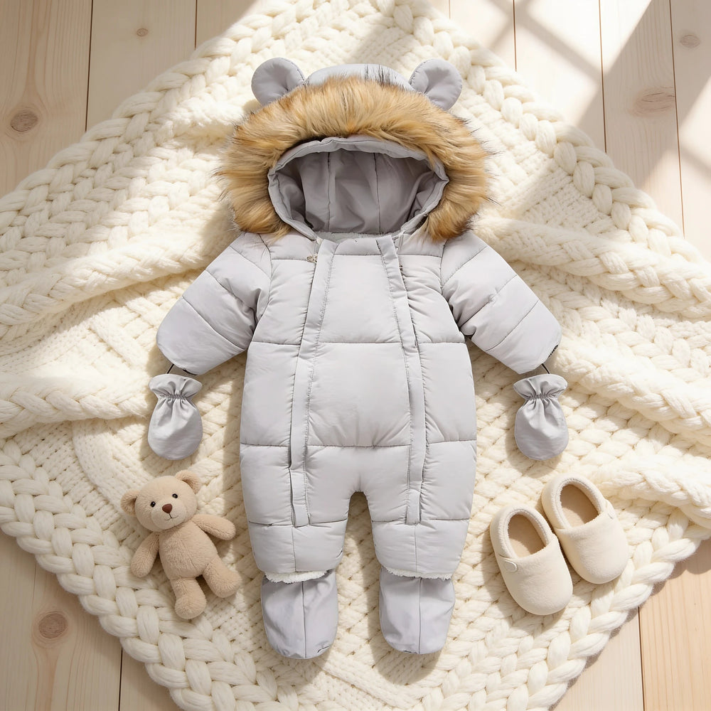 Combinaison Neige Bébé, coloris gris, posée sur un plaid en maille