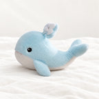 Peluche baleine bleue adorable toute douce posée sur un lit blanc, en pleine lumière