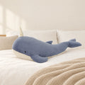 Peluche baleine magique géante bleue posée sur un lit en lin blanc
