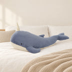 Peluche baleine magique géante bleue posée sur un lit en lin blanc