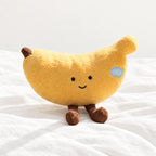 Peluche fruit kawaii banane joviale posée sur un lit blanc, en pleine lumière