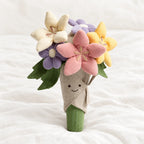 Peluche bouquet de fleurs multicolores kawaii posée sur un lit blanc, en pleine lumière
