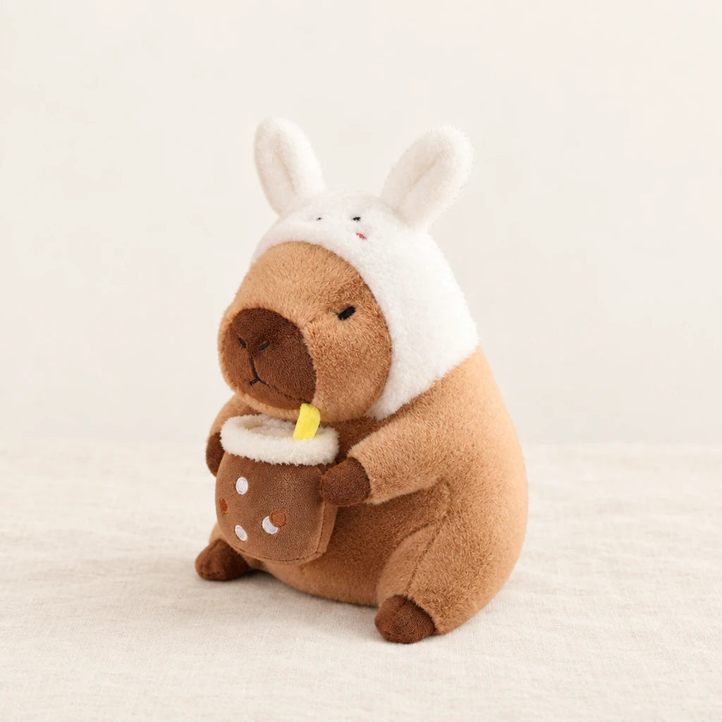 Peluche capybara avec boisson et bonnet rigolo modèle lapin sur fond crème, en studio