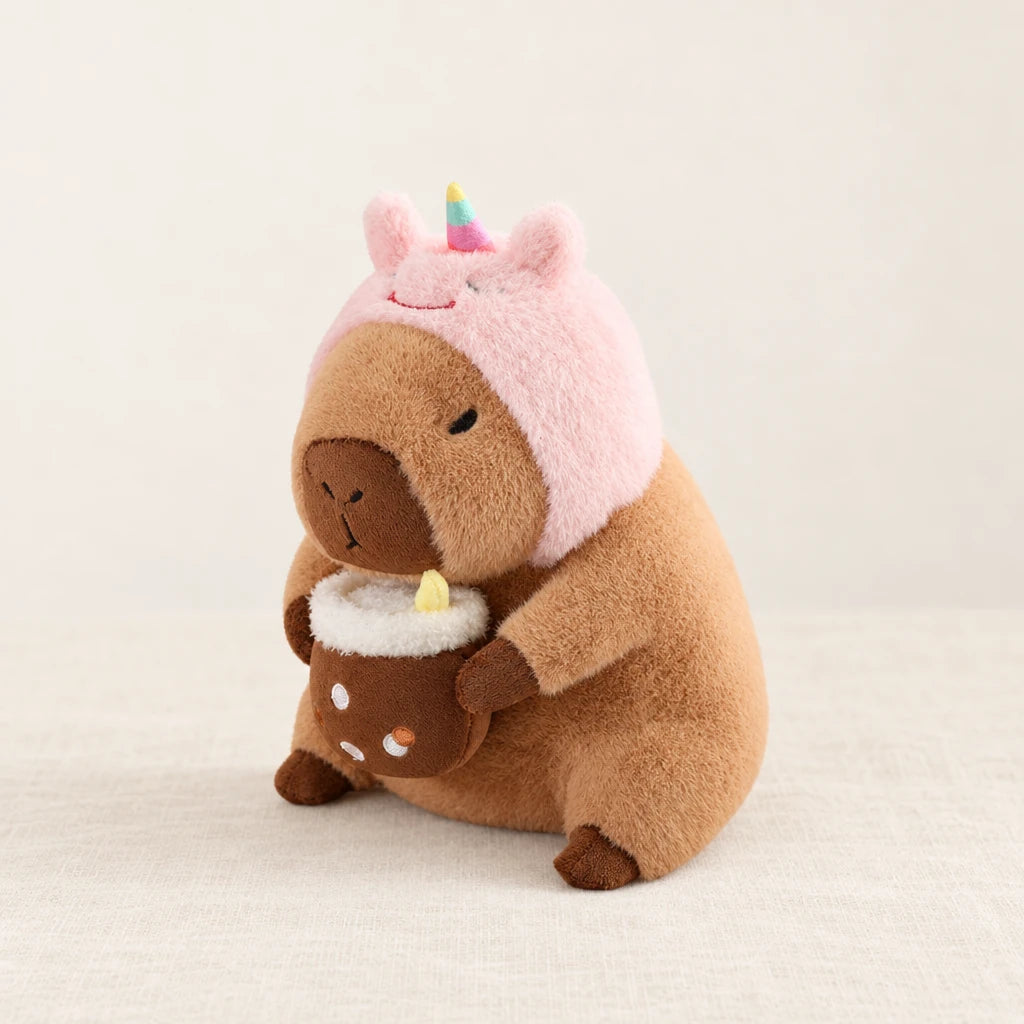 Peluche capybara avec boisson et bonnet rigolo modèle licorne sur fond crème, en studio