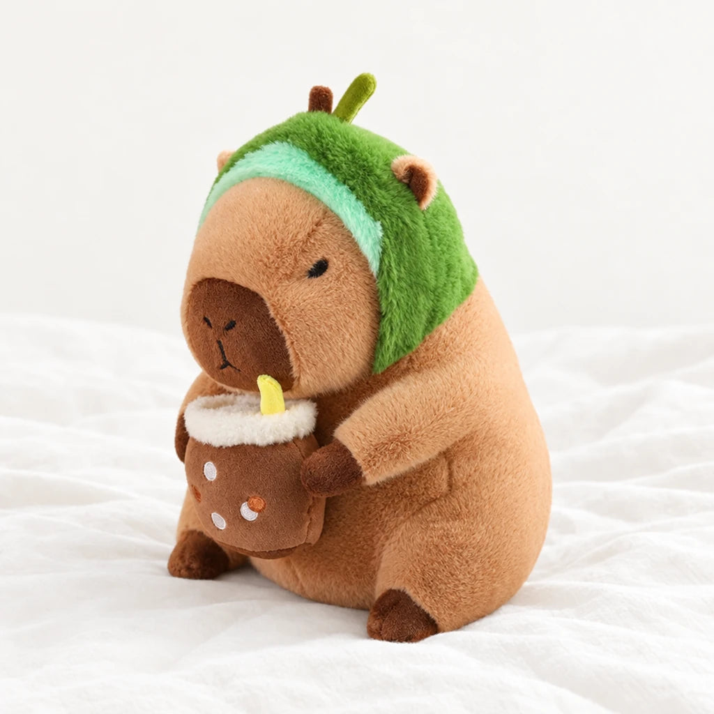 Peluche capybara avec boisson et bonnet rigolo posée sur un lit blanc, en pleine lumière