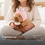 Peluche capybara avec boisson et bonnet rigolo tenue par un enfant pour montrer sa taille réelle. L’animal zen : bonnet à antennes, boisson amovible, dès 3 ans