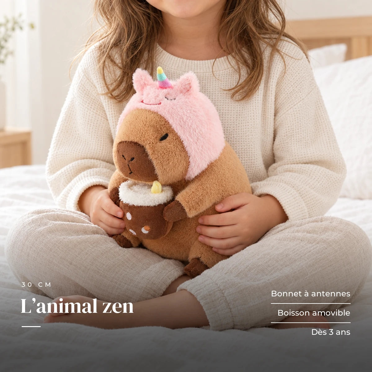 Peluche capybara avec boisson et bonnet rigolo tenue par un enfant pour montrer sa taille réelle. L’animal zen : bonnet à antennes, boisson amovible, dès 3 ans