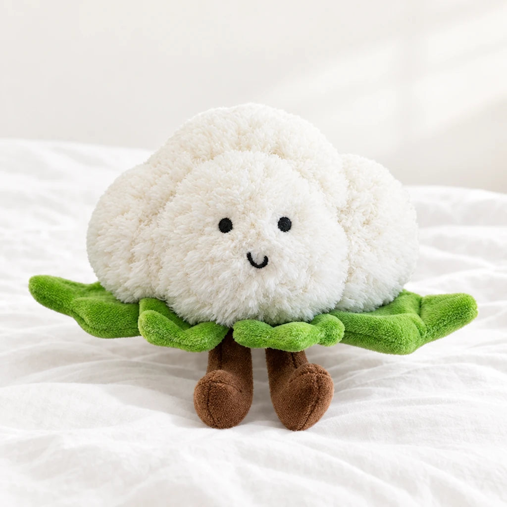 Peluche légume kawaii chou-fleur craquant posée sur un lit blanc, en pleine lumière