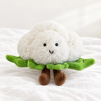 Peluche légume kawaii chou-fleur craquant posée sur un lit blanc, en pleine lumière