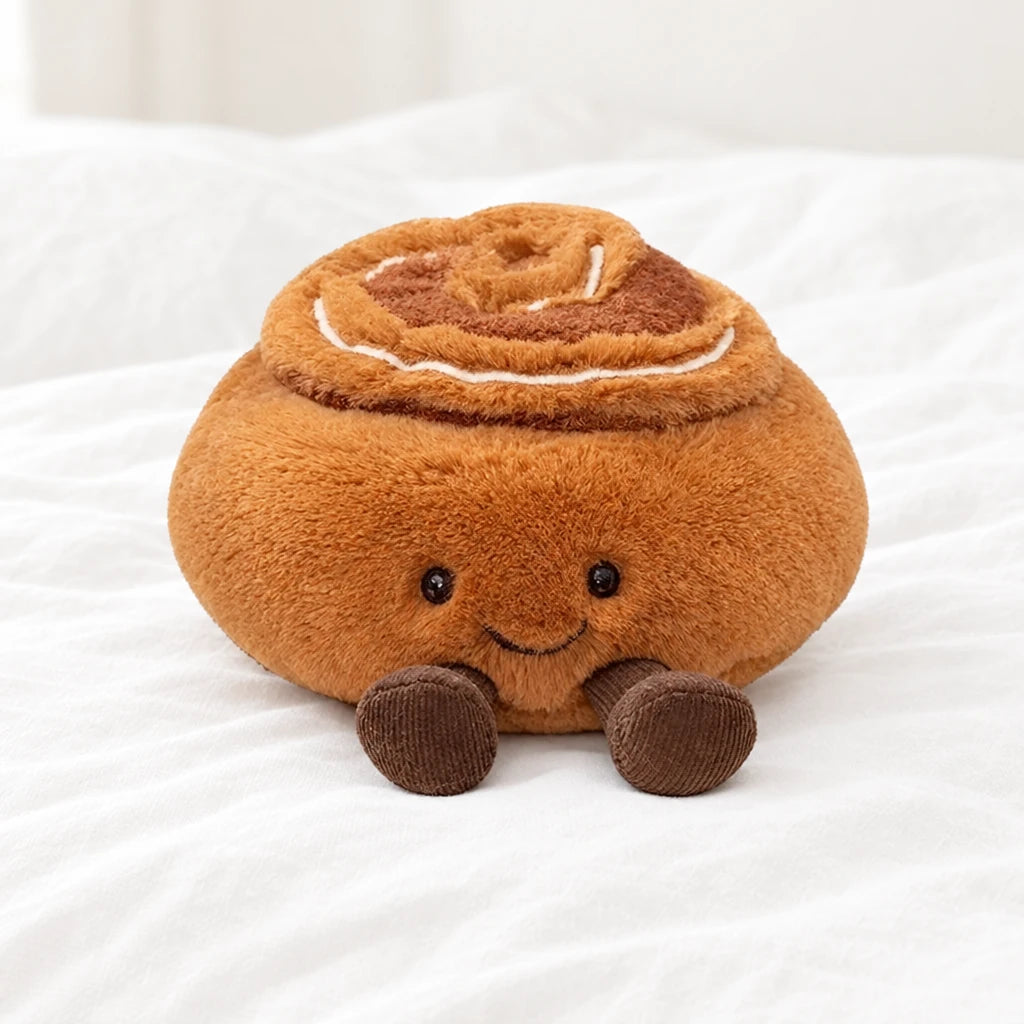 Peluche tea time kawaii cinnamon roll posée sur un lit blanc, en pleine lumière