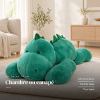 Peluche dinosaure géant relax posée sur un lit en lin blanc. Chambre ou canapé : vert tout doux, format relax, tous âges