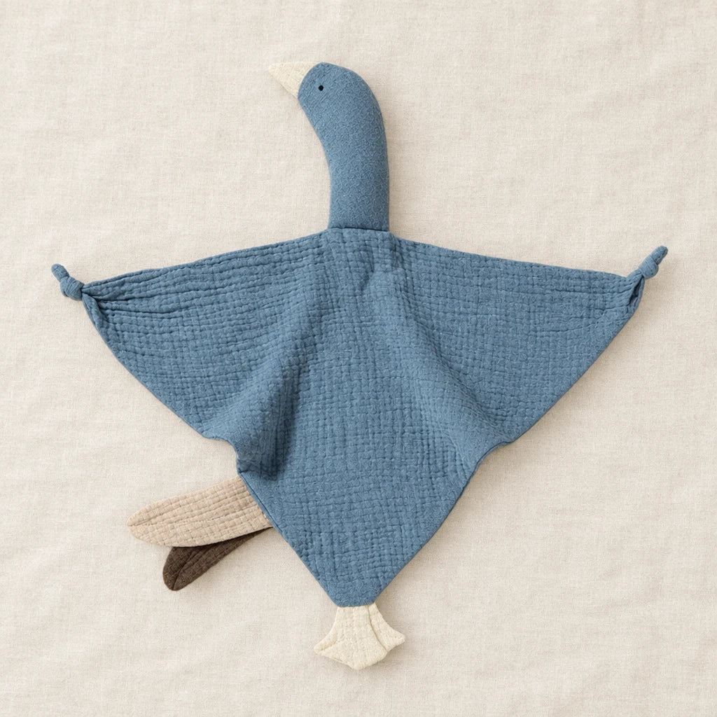 Peluche doudou oie pour bébé en coton bleue présentée à plat sur du lin crème