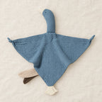 Peluche doudou oie pour bébé en coton bleue présentée à plat sur du lin crème