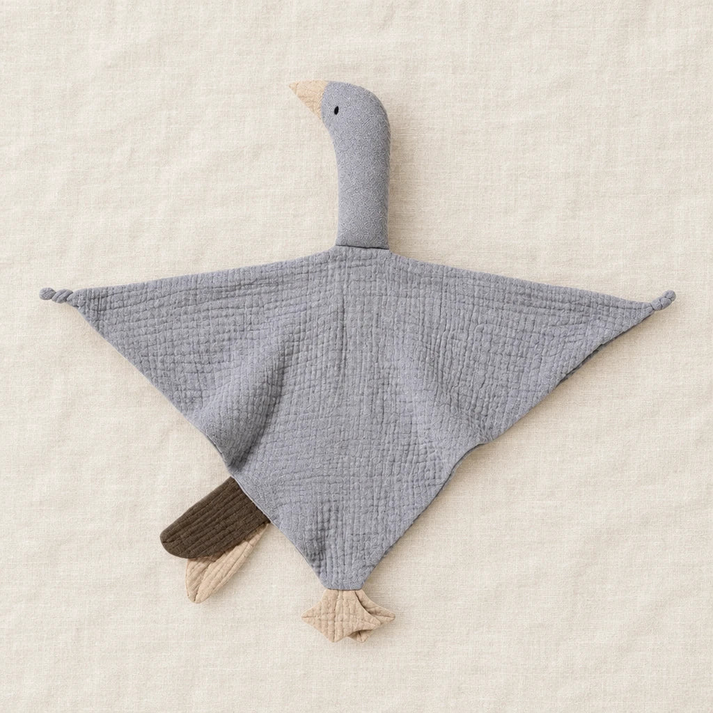 Peluche doudou oie pour bébé en coton grise présentée à plat sur du lin crème