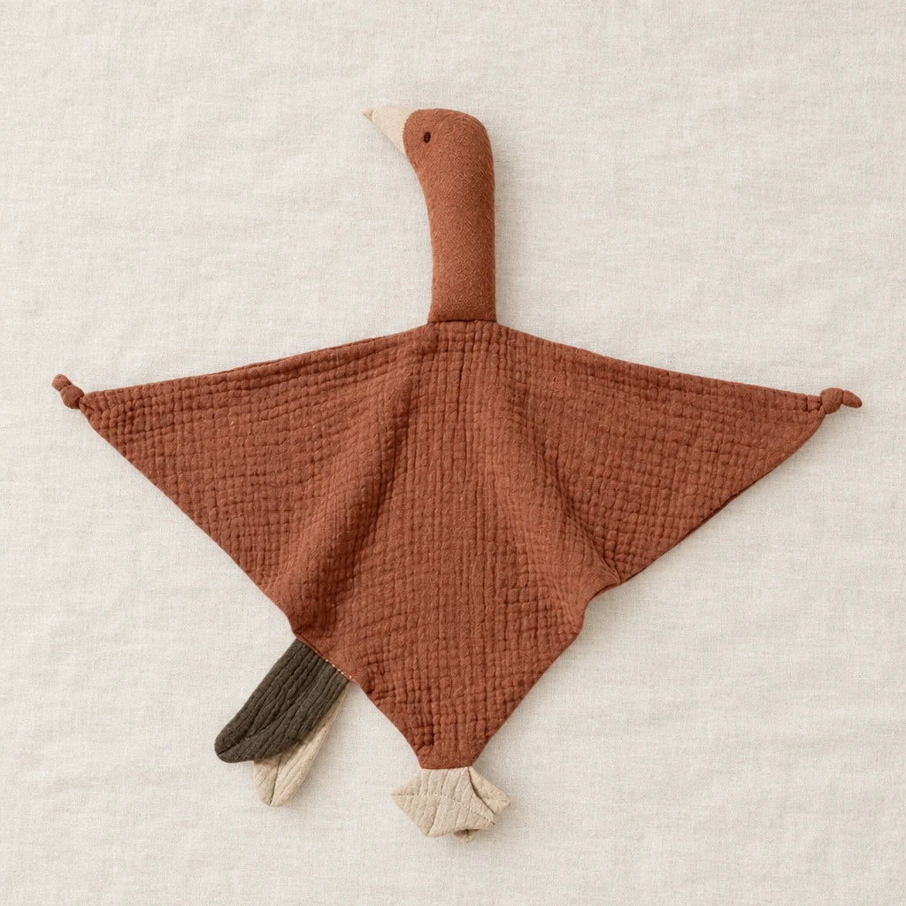 Peluche doudou oie pour bébé en coton marron présentée à plat sur du lin crème