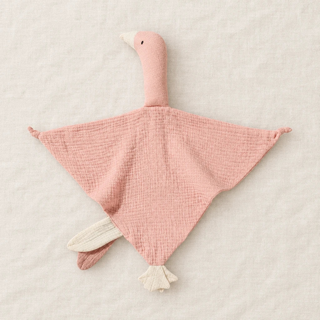 Peluche doudou oie pour bébé en coton rose présentée à plat sur du lin crème