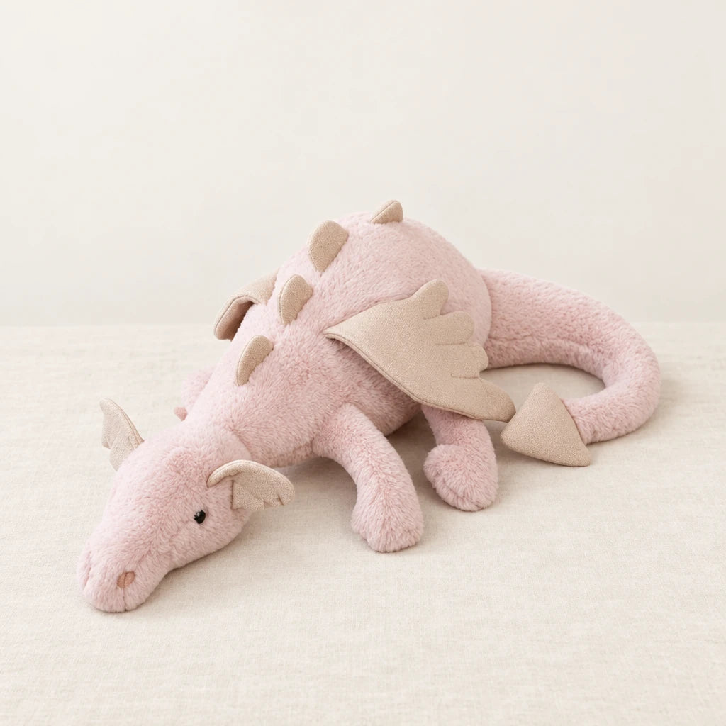 Dragon en peluche aux couleurs pastel rose posé sur un lit en lin blanc