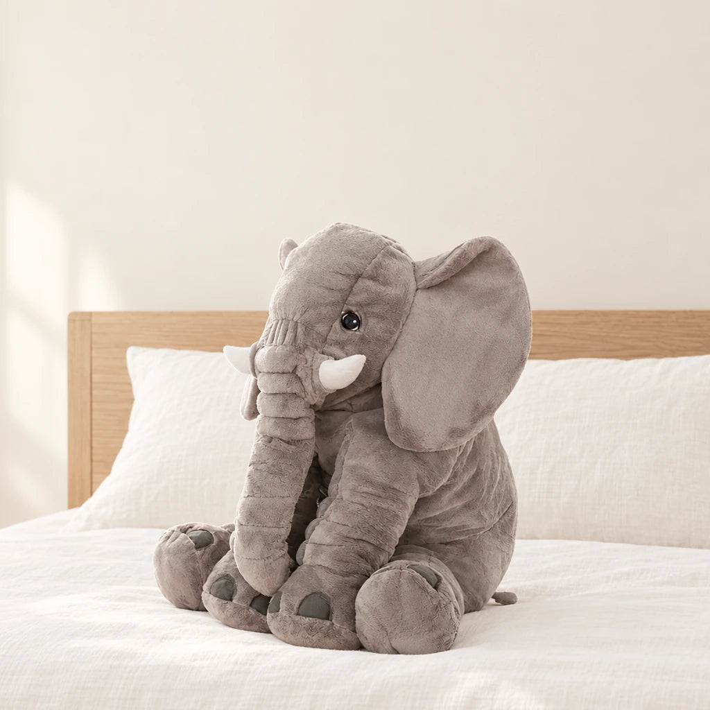 Peluche éléphant oreiller grise posée sur un lit en lin blanc
