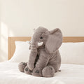Peluche éléphant oreiller grise posée sur un lit en lin blanc