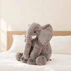Peluche éléphant oreiller grise posée sur un lit en lin blanc