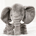 Peluche éléphant oreiller grise posée sur un lit blanc, en pleine lumière