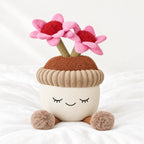 Peluche kawaii fleurs en pot de terre posée sur un lit blanc, en pleine lumière